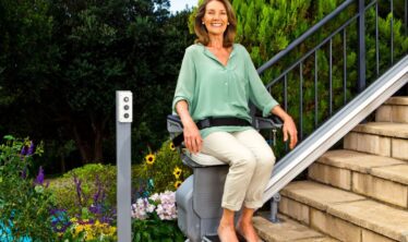 Happy woman sat on an outdoor stairlift for straight stairs.