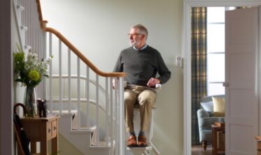 A man is going up the stairs with a Stannah stairlift for curved stairs