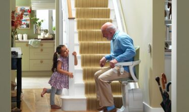 Senior man sat on his Stannah stairlift looking at his granddaughter, smiling.