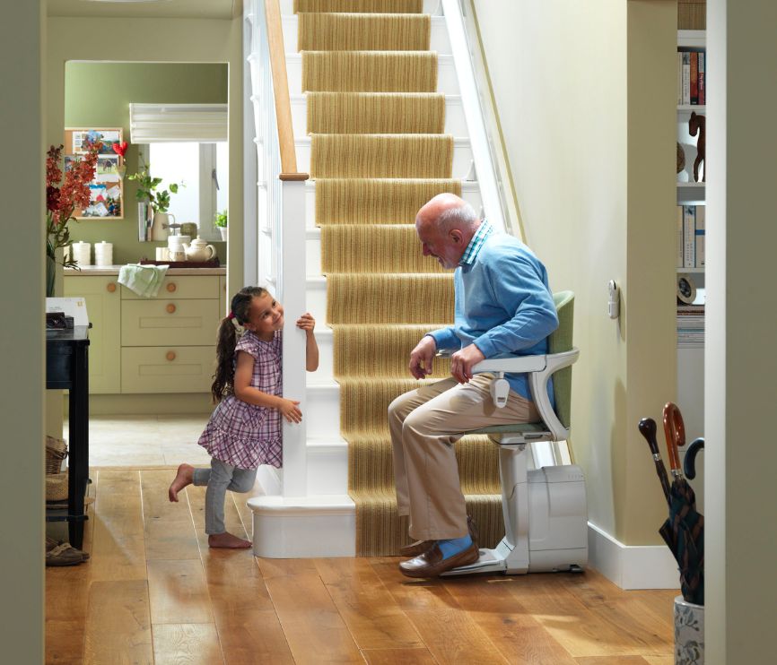Senior man sat on his Stannah stairlift looking at his granddaughter, smiling.