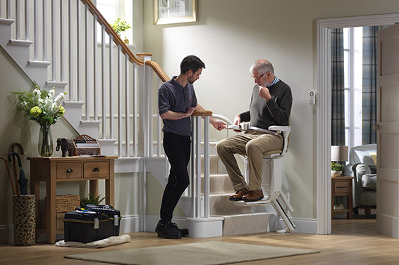 Technician explaining to a man how to use the stairlift while he’s sitting on it. 