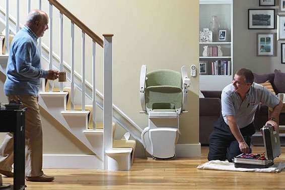 Stannah technician servicing a stairlift maintenance. The senior man is watching the process, smiling. 
